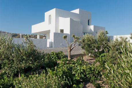 A modernist white building with geometric shapes, surrounded by lush greenery.