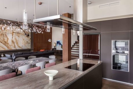 A modern open-concept kitchen and living area with marble countertops, sleek lighting, and a floating staircase.