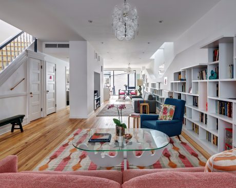 Vibrant open-concept living space with modern chandelier, bookshelves, and glass coffee table.