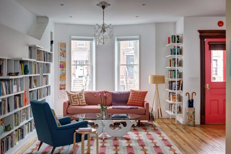 Bright, eclectic living room with built-in bookshelves, crystal chandelier, and vibrant red door.