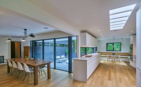 Spacious open-plan living room with large windows, wooden dining table, and sleek kitchen.