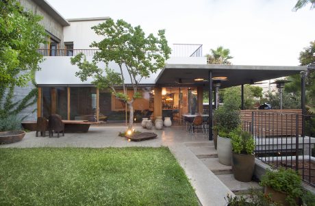 A modern outdoor living space with a covered patio, lush greenery, and a fire feature.