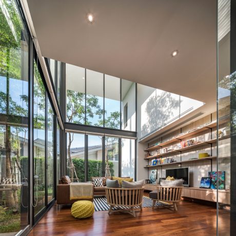 Bright, modern living room with large windows, wooden furniture, and built-in shelves.