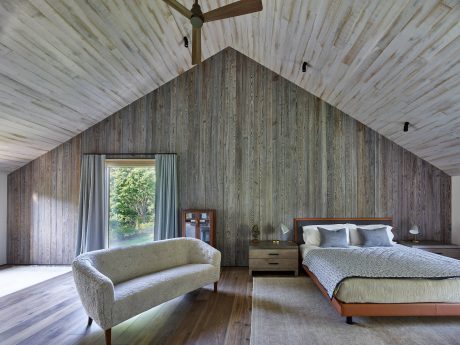 Rustic bedroom with vaulted wooden ceiling, gray plank walls, and modern furnishings.