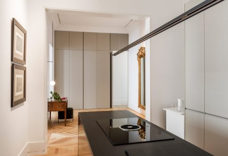 A modern and minimalist interior design with sleek cabinets, a black countertop, and a gilded mirror.