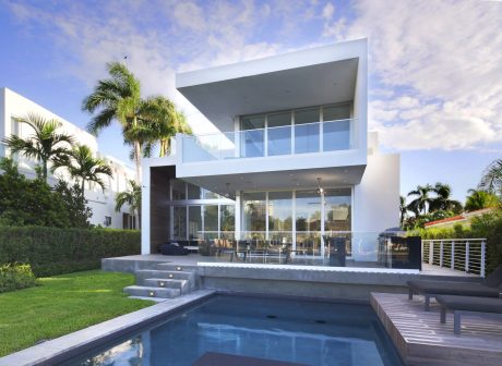 A modern, two-story residence with expansive glass walls, a pool, and lush tropical landscaping.