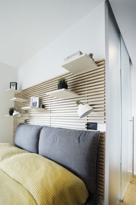 A modern living space with a slatted wood wall, shelving, and a cozy gray couch.