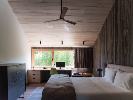 A cozy bedroom with a wooden ceiling, large windows, and a modern, minimalist decor.