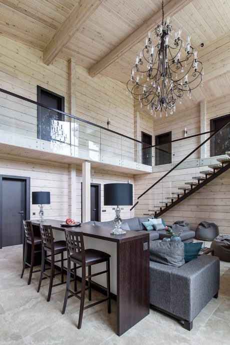 Elegant wooden chalet interior with a grand chandelier and glass balcony above.