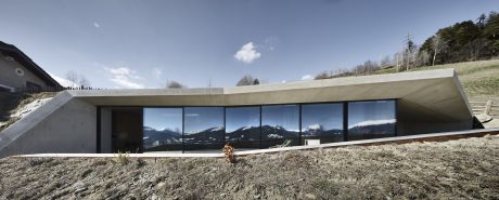 A modern, low-profile building with a sweeping glass facade showcasing mountain scenery.