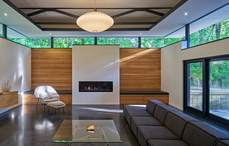 A modern, open-concept living space with floor-to-ceiling windows, a fireplace, and warm wood accents.