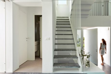 Modern minimalist foyer with white walls, marble stairs, and glass railing.