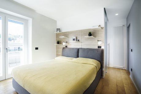 Modern bedroom with slatted wooden shelving, gray upholstered bed, and yellow quilt.