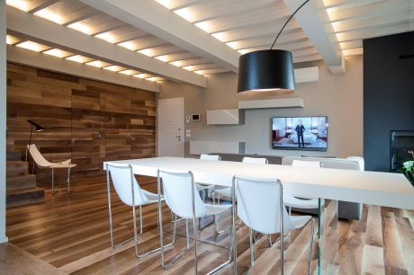 A modern, open-concept dining area with wooden accents, sleek white furniture, and a large TV.
