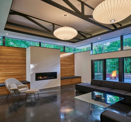 Inviting modern living space with wood paneling, fireplace, and large windows overlooking nature.