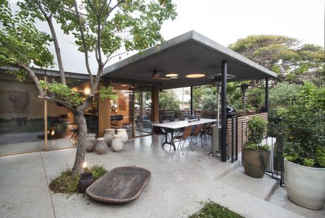 Modern open-air dining area with concrete floor, glass walls, and a covered patio structure.