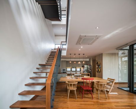 Modern open-plan kitchen and dining area with wooden stairs, pendant lights, and large windows.