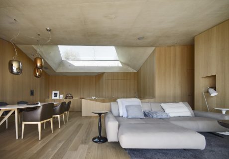 Spacious open-plan living area with modern wooden paneling, large skylight, and minimalist furnishings.