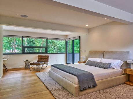 Spacious modern bedroom with floor-to-ceiling windows, wood floors, and plush furnishings.