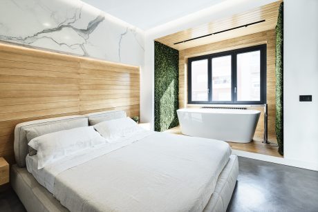 Sleek, modern bedroom with wooden walls, marble accent, and freestanding bathtub.