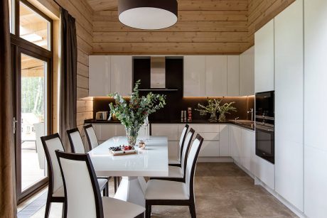 Rustic cabin interior with modern kitchen, dining table, and natural wood ceiling.