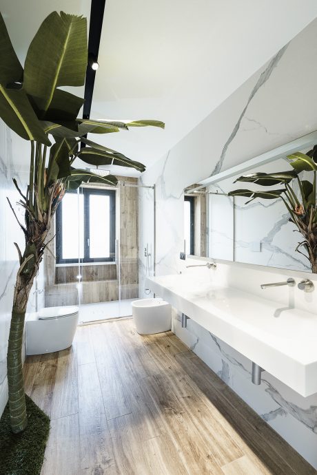 Sleek bathroom design with lush tropical plants, marble walls, and a spacious vanity.