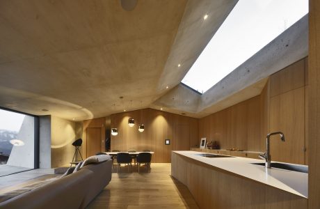 Spacious open-plan kitchen and living area with concrete ceiling and wood paneling.