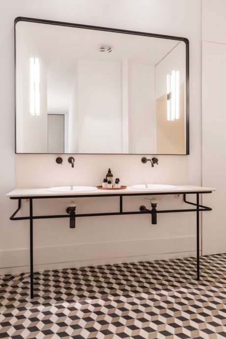 Modern bathroom design with a large mirror, double sink vanity, and geometric tile flooring.