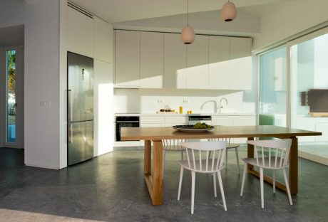 Minimalist kitchen with sleek white cabinets, wooden dining table, and pendant lighting.