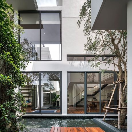 A modern home with a glass façade, indoor pond, and tree inside the courtyard.