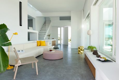 Spacious modern living room with minimalist decor, concrete floors, and floor-to-ceiling windows.