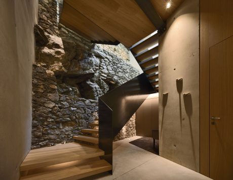 A modern, minimalist staircase with wooden steps and a stone feature wall, creating a dramatic entryway.