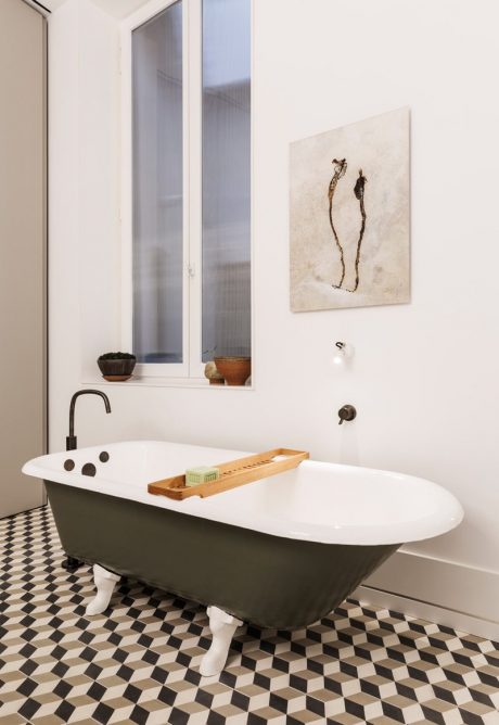 A modern bathroom with a clawfoot tub, checkered tile floor, and abstract artwork.