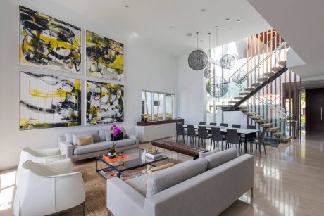 Spacious contemporary living room with abstract artwork, pendants, and wood-and-glass staircase.