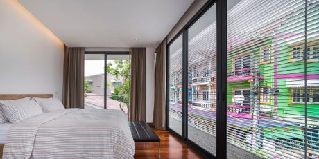 A modern bedroom with large floor-to-ceiling windows overlooking a vibrant, colorful urban setting.