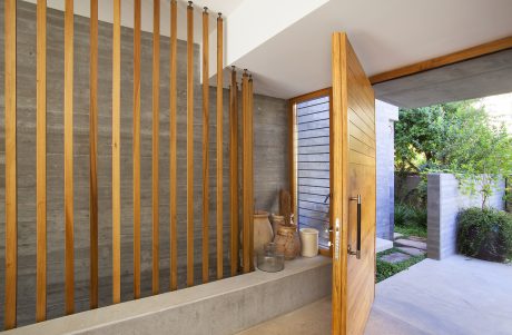 Wooden slats, concrete walls, and natural landscaping create a modern, earthy entryway.