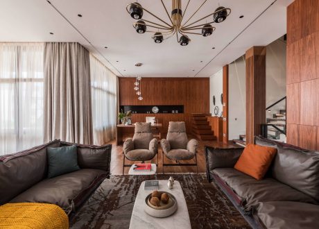 Luxurious living room features wooden walls, modern chandelier, and plush seating.
