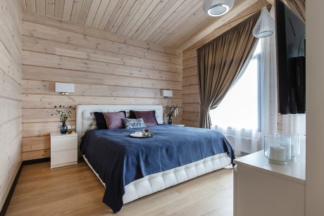 A cozy wooden bedroom with a plush bed, pendant lights, and a curtained window.