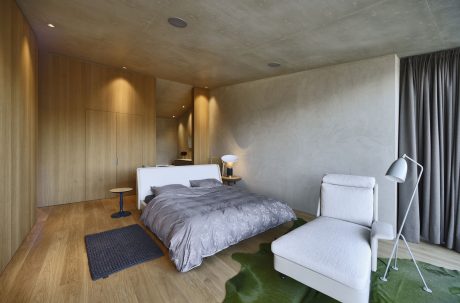 A modern, minimalist bedroom with wooden walls, a large bed, and a cozy armchair.