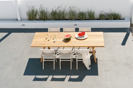 A minimalist outdoor terrace with a wooden dining table, white chairs, and potted plants.