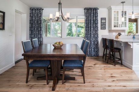 A modern, open-concept dining room with wooden table, navy blue chairs, and patterned curtains.