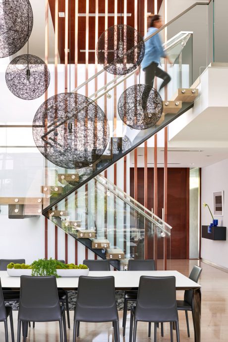 Striking modern interior with intricate wire spheres, glass staircase, and natural elements.