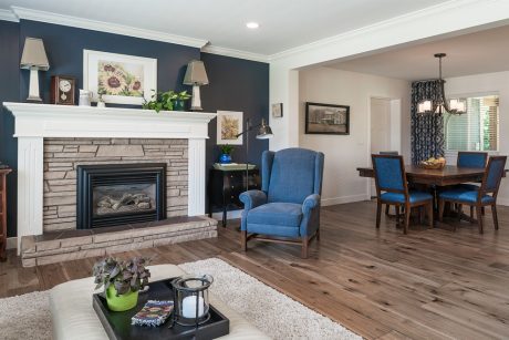 A cozy living room with a stone fireplace, blue chairs, and a wooden dining table surrounded by dark walls.