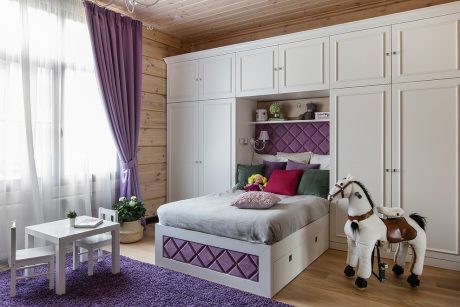 A cozy bedroom with wooden walls, built-in cabinets, and a vibrant purple and white decor.