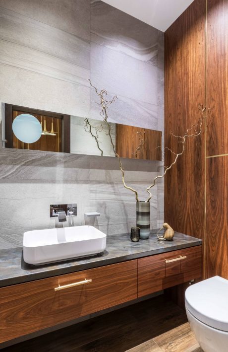 Sleek bathroom design featuring marble walls, wooden vanity, and sculptural decor.