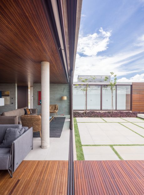A modern open-concept living space with concrete walls, wood ceilings, and a lush courtyard view.