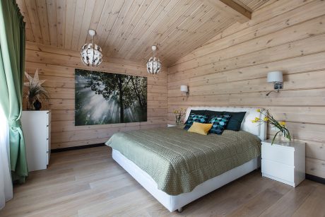 Cozy wooden cabin bedroom with plank walls, pendant lights, and a large nature image on the wall.