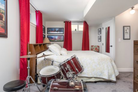 A cozy bedroom with a drum set, shelves, and red curtains creating a music-inspired ambiance.