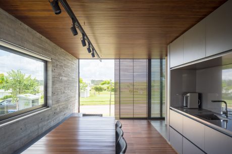 Modern open-concept kitchen with concrete walls, wood ceiling, and floor-to-ceiling windows.