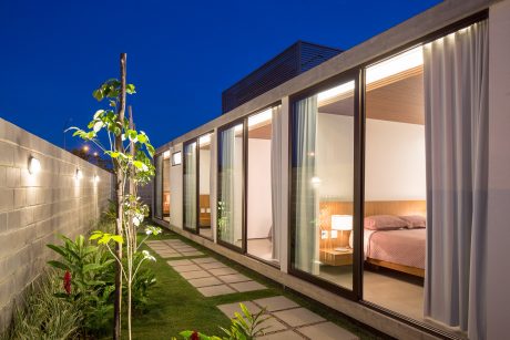 Sleek modern villa with large windows, landscaped path, and lush greenery at night.